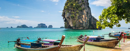 Long tail boats moored on a golden sand beach with limestone islands in the tropical Phang Nga Bay in Thailand.