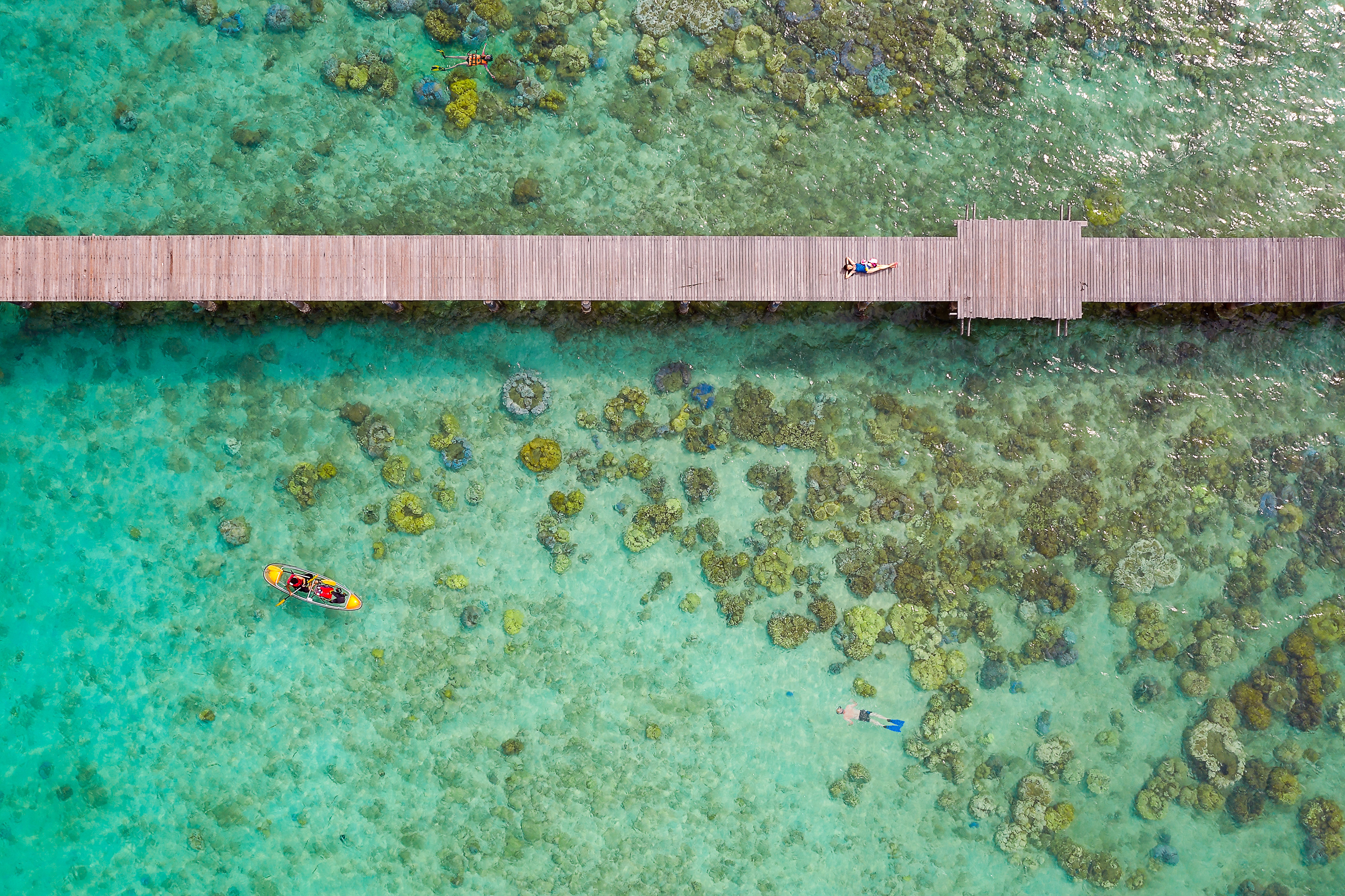 Aerial view woman lying on a pier over tropical shallow reef with canoeist at Koh Kood island in Thailand.