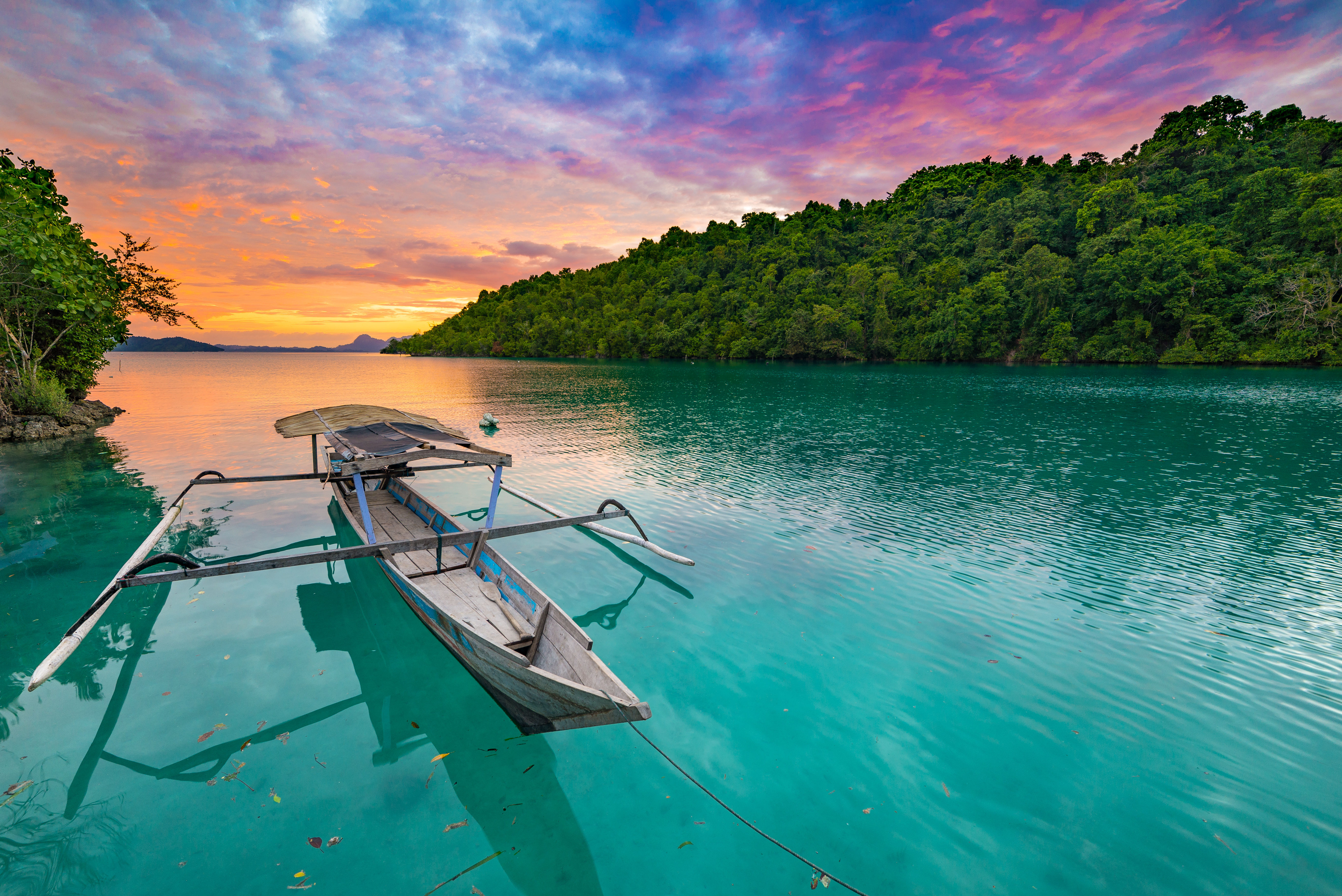 Traditional Indonesian boat floating on blue green lagoon in the Togean Islands, Sulawesi at sunset. 