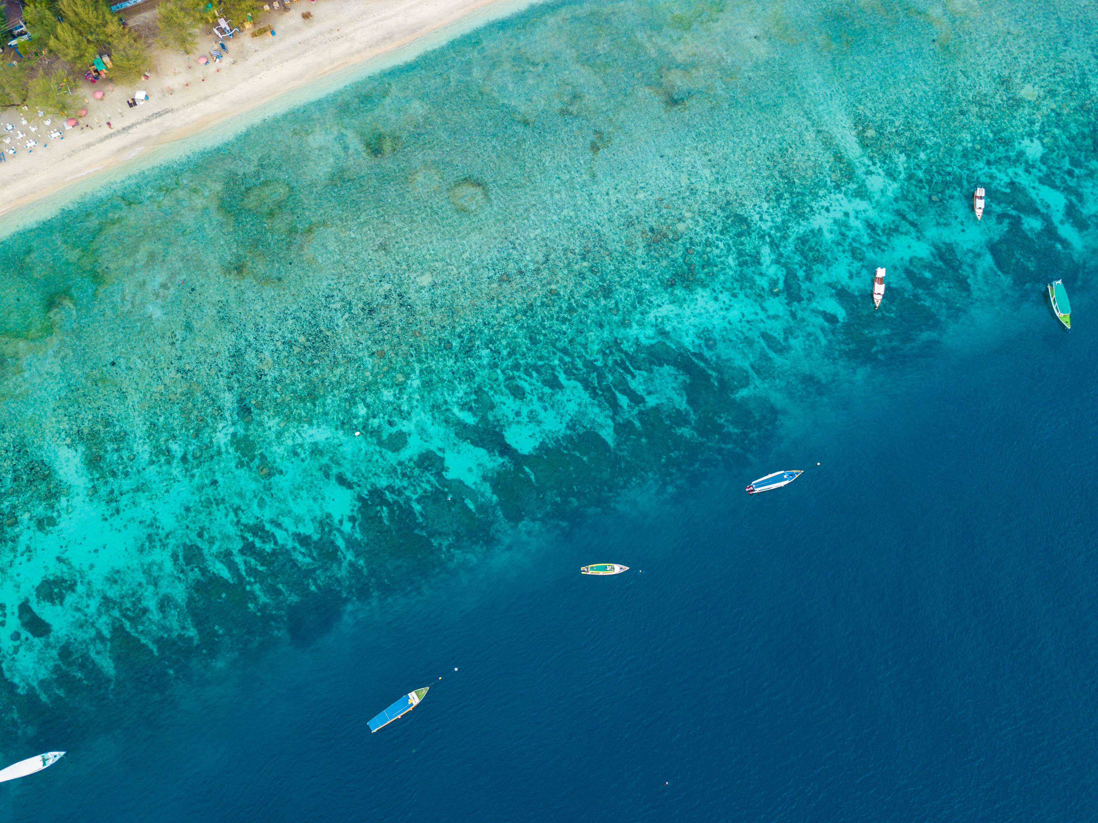 Aerial view of Gili Island coastline with boats, white sand and turquoise waters, West Nusa Tenggara, Indonesia.