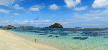 White sand tropical beach with shallow reef and blue skies in Moyo Indonesia. 