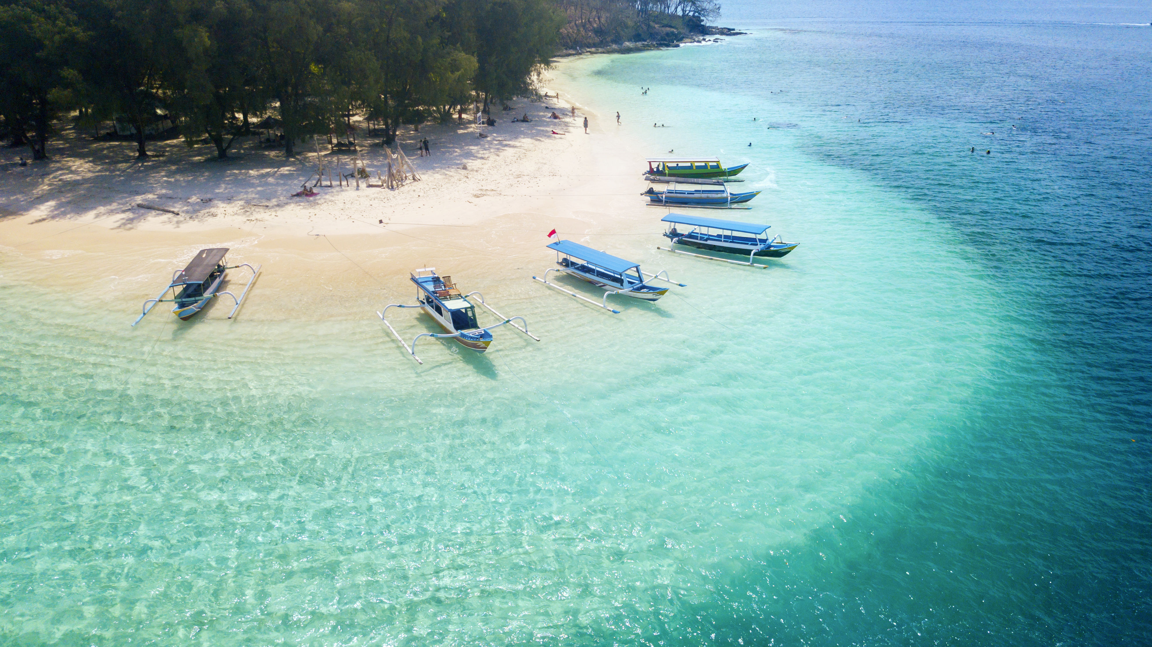 Traditional Indonesian canoe boats (Jukung) mored on tropical turquoise shore with white sand beach at Gili Islands.