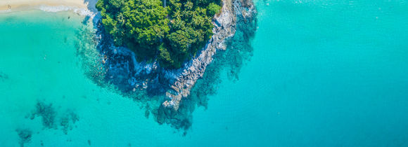 Tropical island outcrop with rocks and palm trees, surrounded by turquoise waters in South East Asia. 