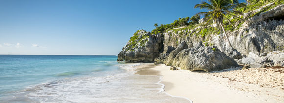 White sand tropical beach with palm trees and rocks in Tulum, Mexico.