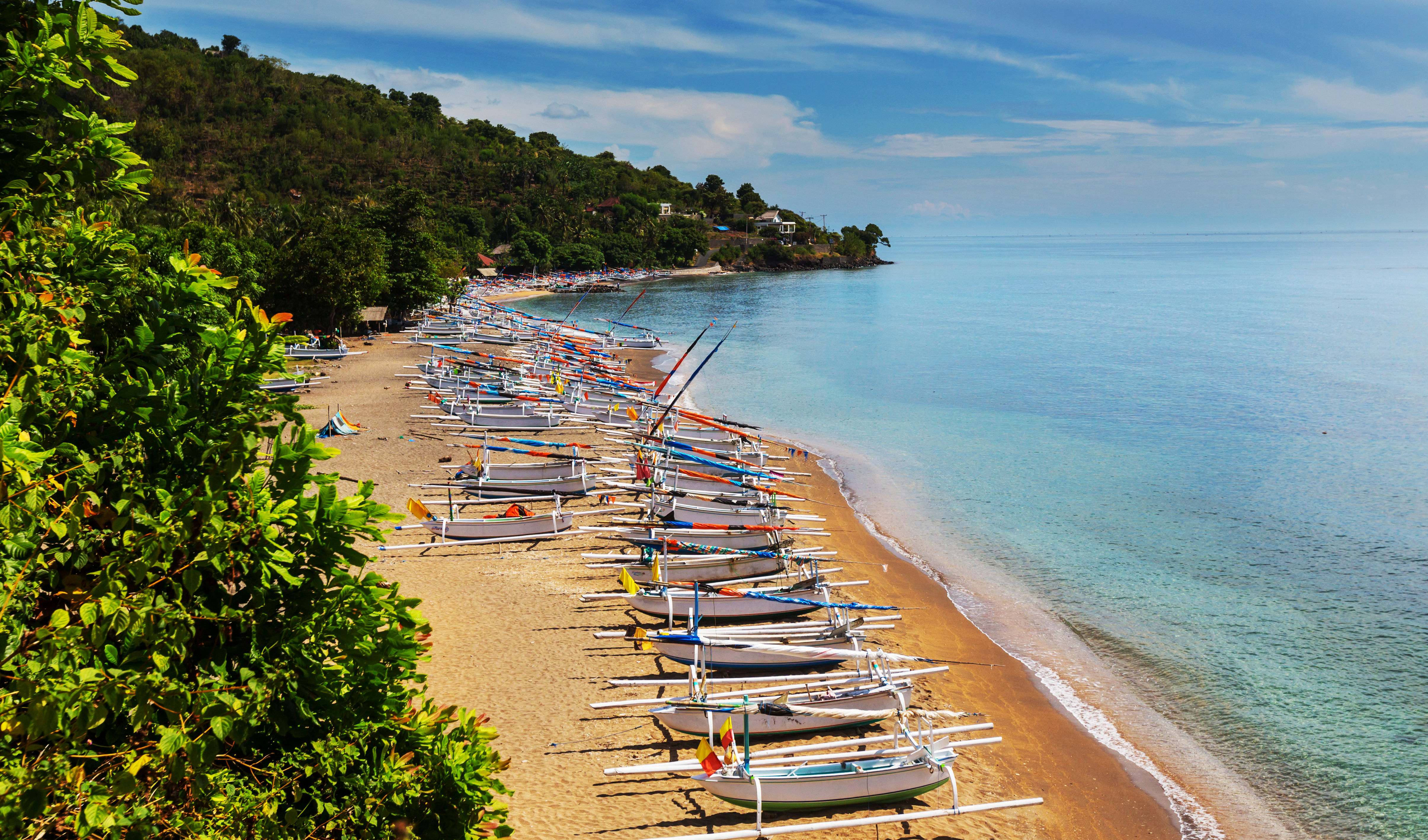 Traditional Indonesian wooden boats lined up on a golden sand beach at Amed, Bali.