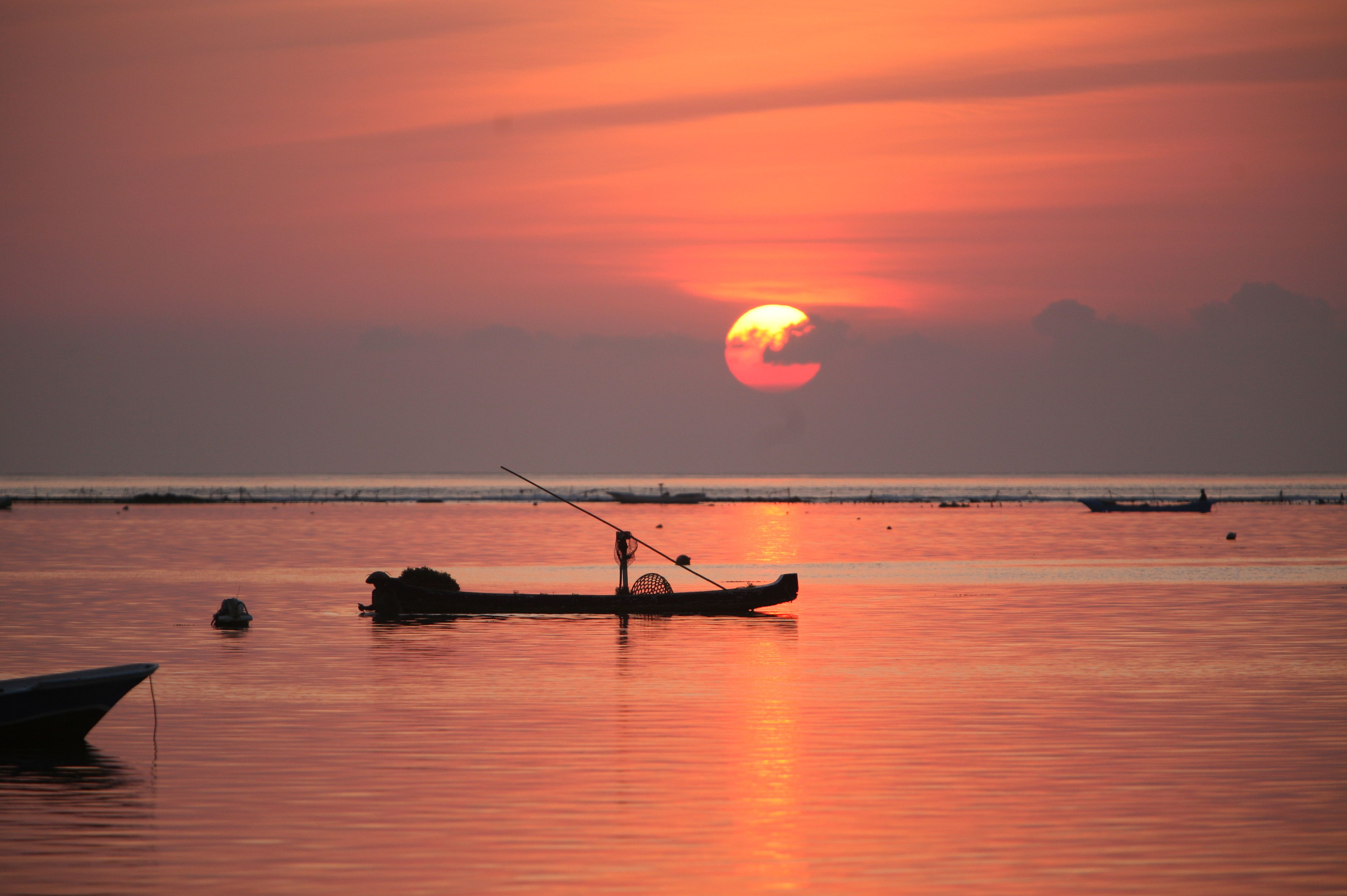 Indonesian boats on flat sea at red sky sunset in Nusa Lembongan, Bali.