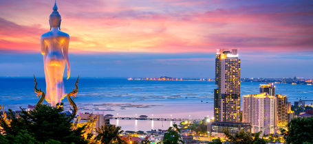 Panoramic view overlooking Pattaya bay at at sunset with purple and pink sky, huge standing big Buddha and hotels.