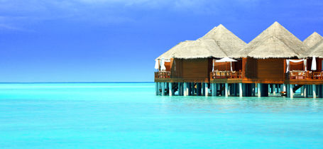 Wooden bungalows over turquoise waters of Kaafu Atoll in the Maldives.