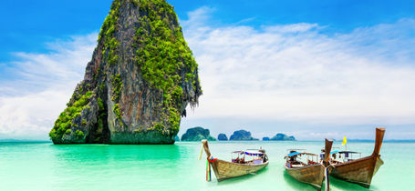 Three traditional longtail boats on turquoise water next to limestone rock in Krabi. 