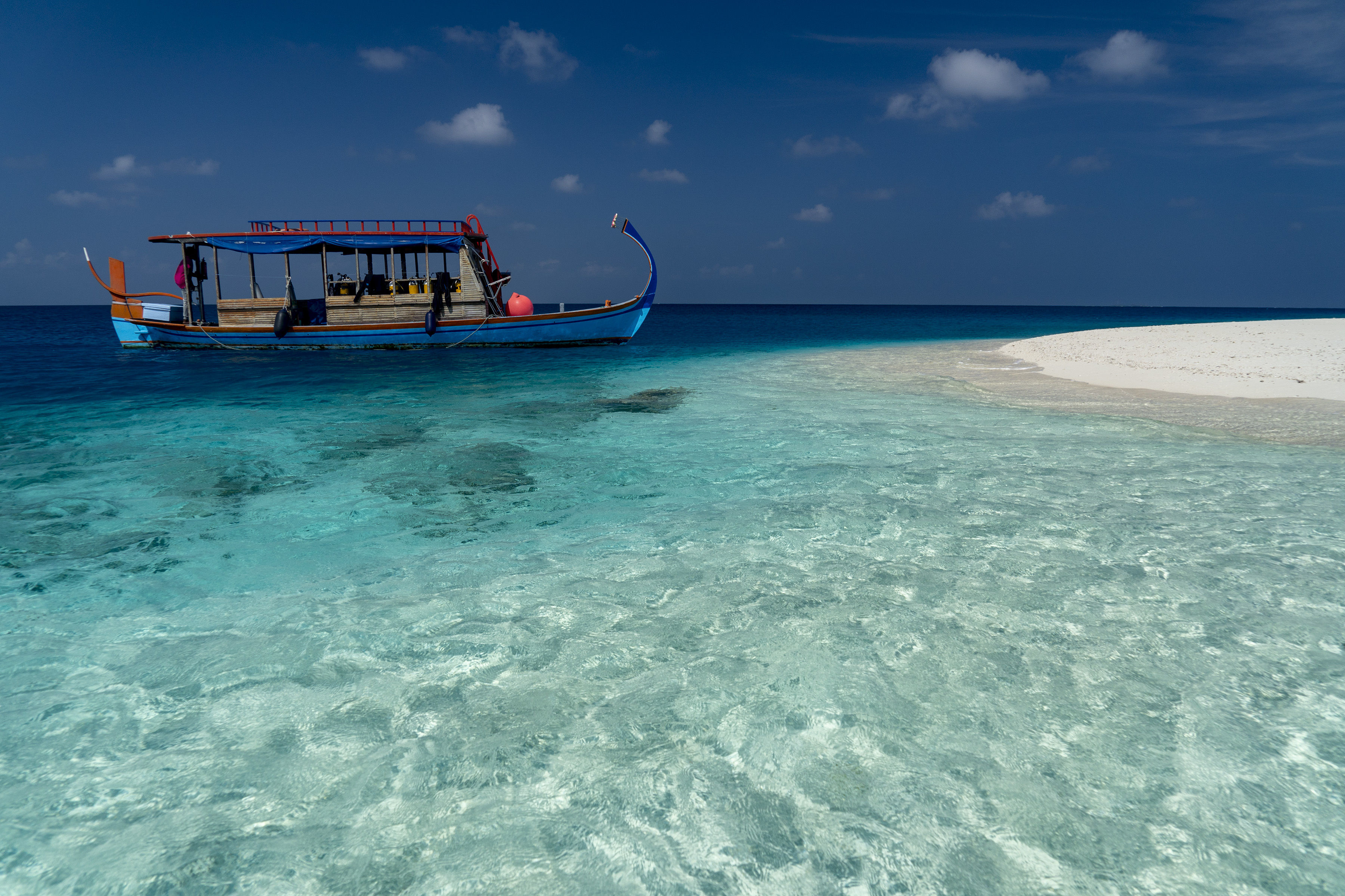 Traditional Maldivian Dhoni next to white sand island in Central Atoll on tropical turquoise waters.