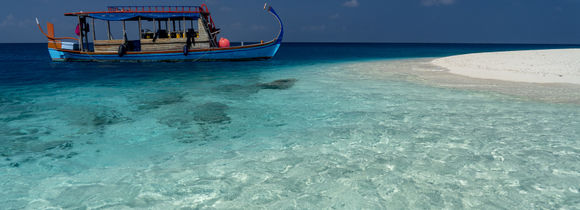 Traditional Maldivian Dhoni next to white sand island in Central Atoll on tropical turquoise waters.