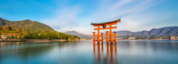 Miyajima Island and the famous Floating Torii gate on blue water, green hills and blue skies. 