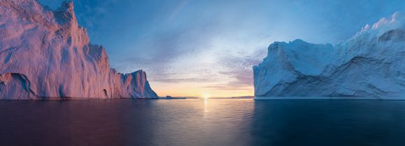 Midnight sun rising in between two icebergs in Antarctica. 