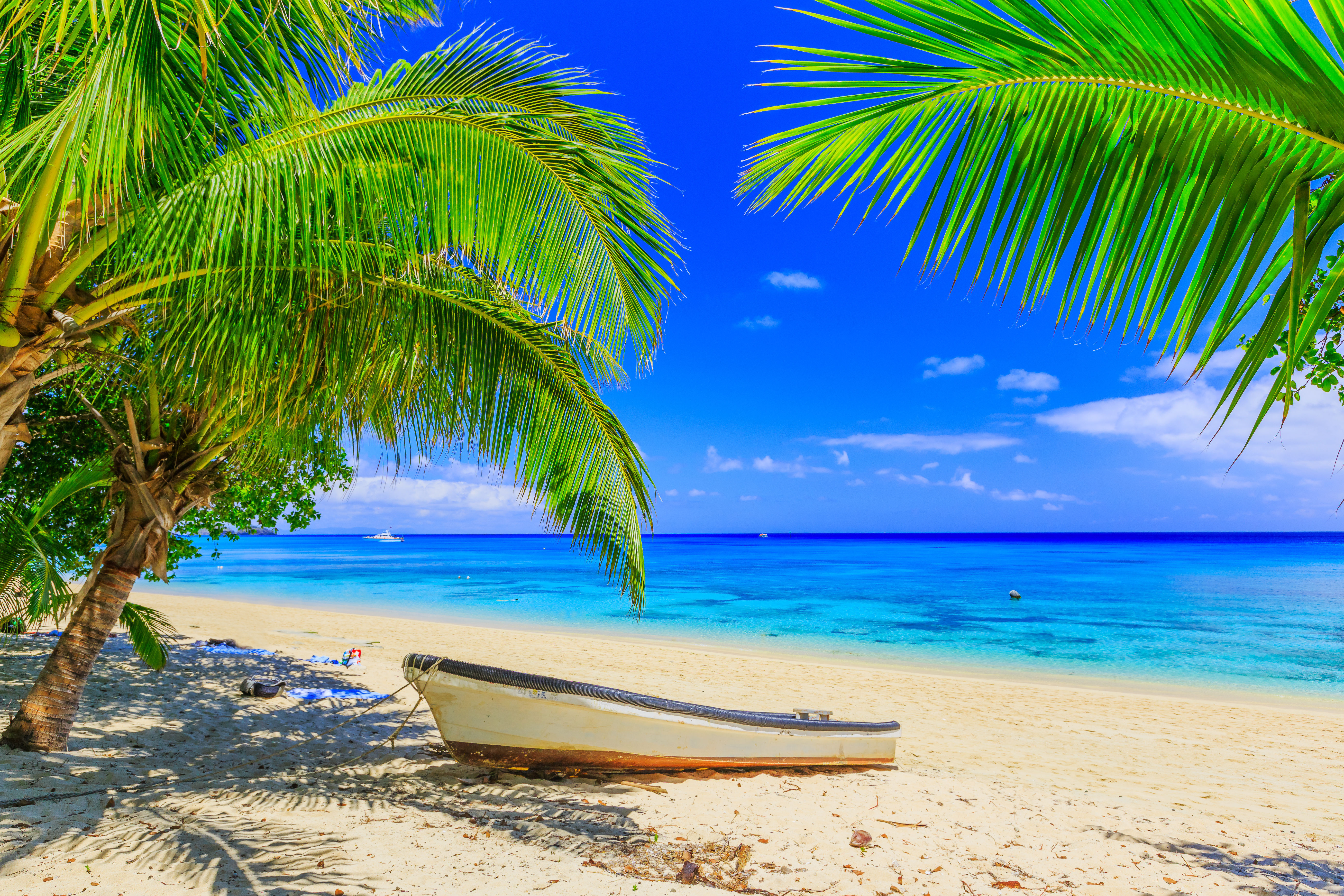 Small white wooden boat on white sand beach with palm trees and turquoise waters in Fiji.