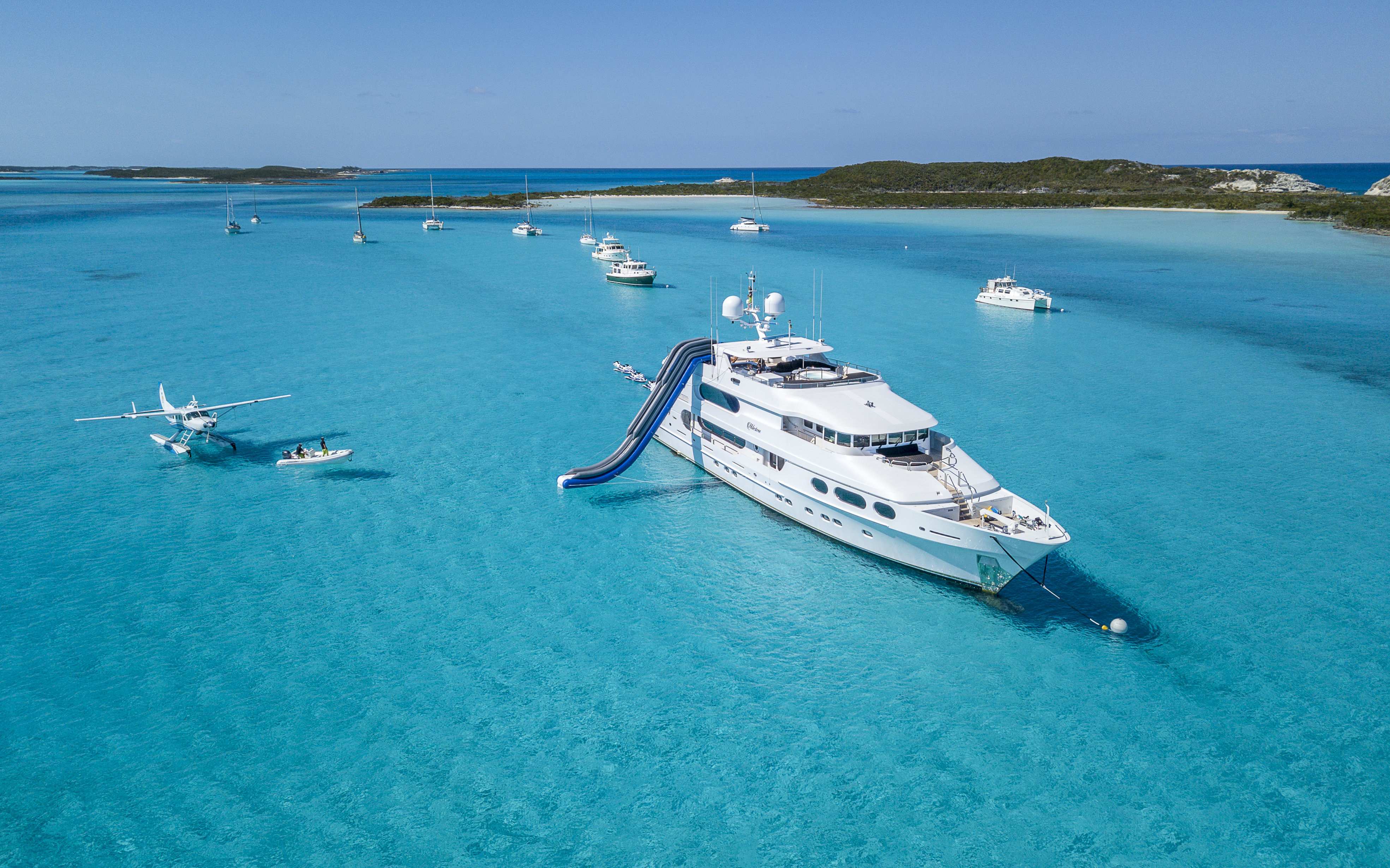White yachts and sea plane on azure blue waters near islands in the Bahamas.