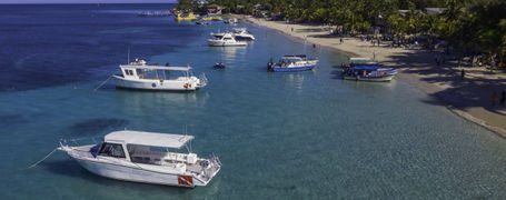Small white scuba diving boats on clear turquoise waters next to beach in Honduras. 