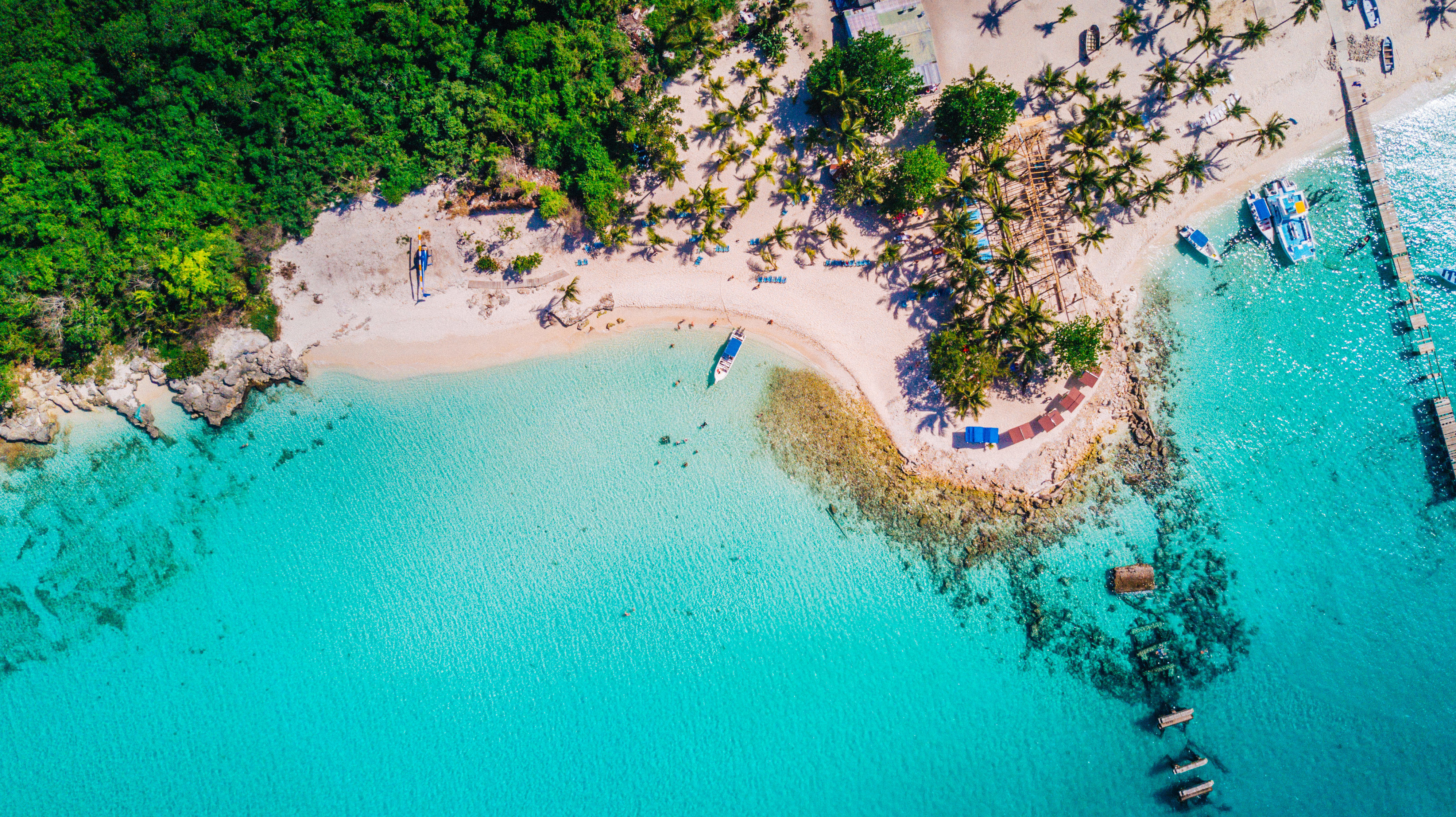 Aerial drone view of reef, trees and beach in a tropical landscape with boats in Dominican Republic.