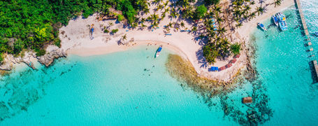 Aerial drone view of reef, trees and beach in a tropical landscape with boats in Dominican Republic.