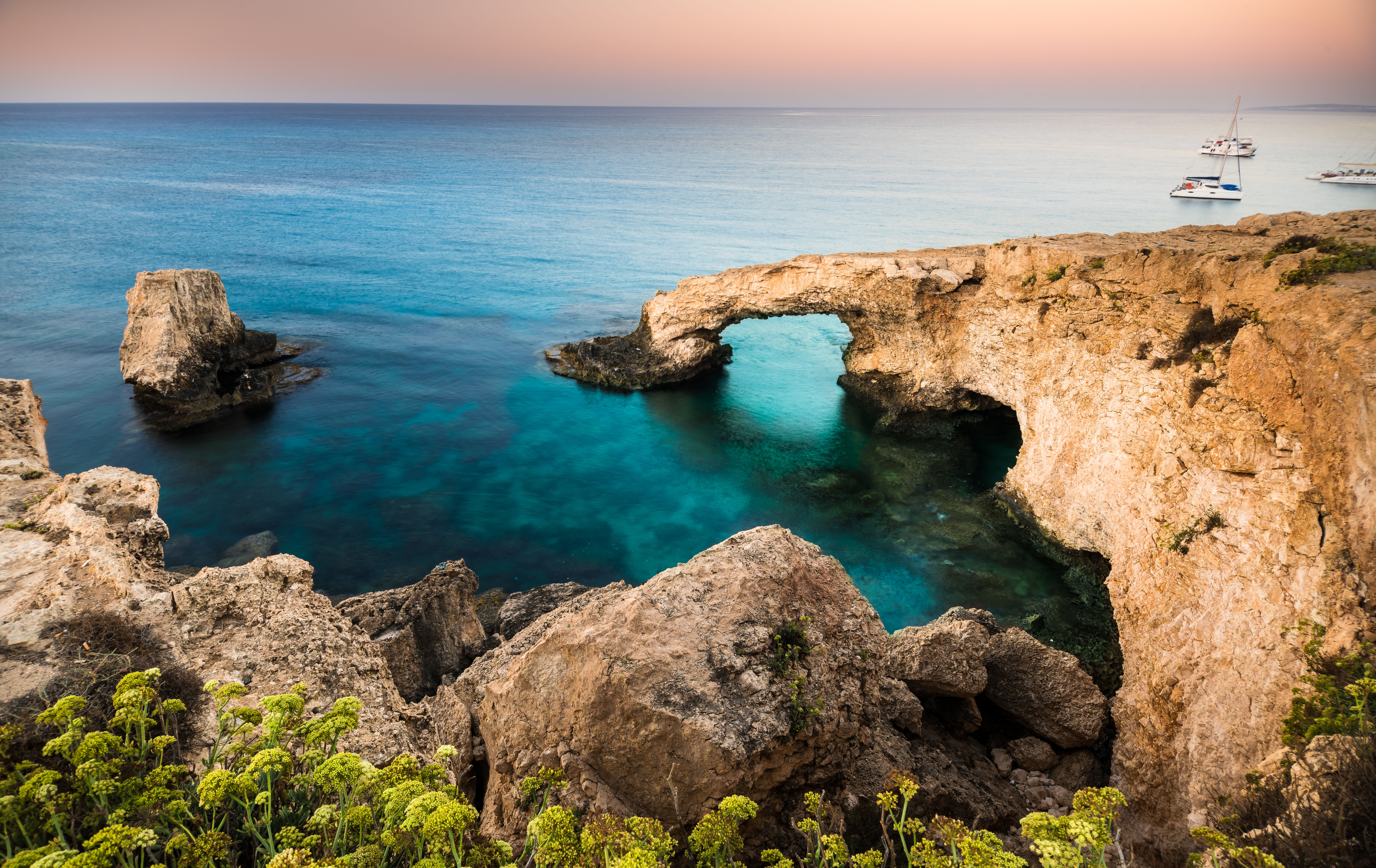 Natural rock arch in over green and blue waters at sunset on Cyprus island.