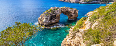 Natural rock arch out on turquoise waters and blue skies in Spain.