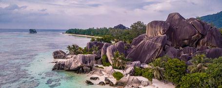 Granite boulder rocks on white sand beach next to shallow reef in Seychelles.  