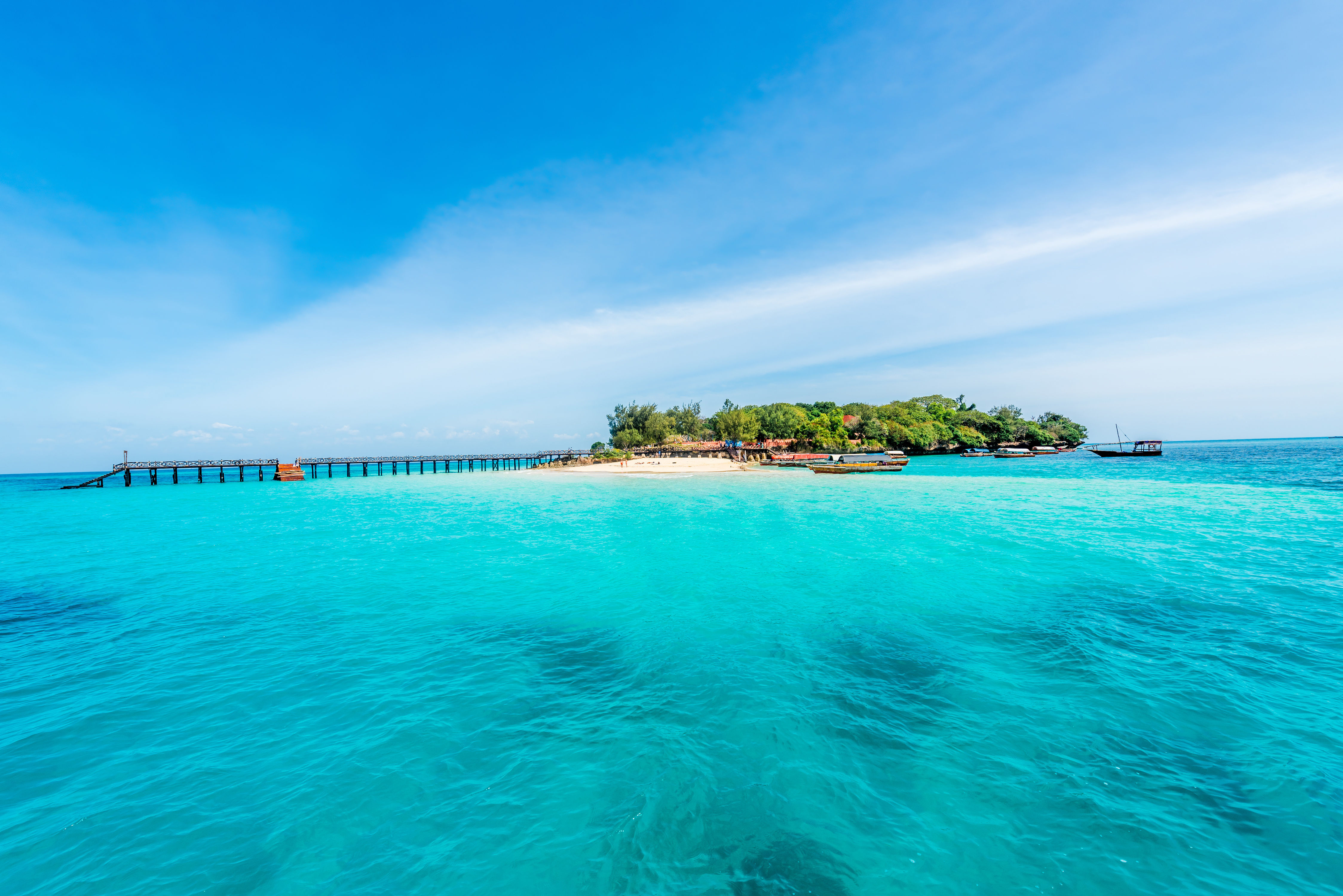 Small tropical island with wooden jetty, surrounded by turquoise waters and clear blue skies off Madagascar. 