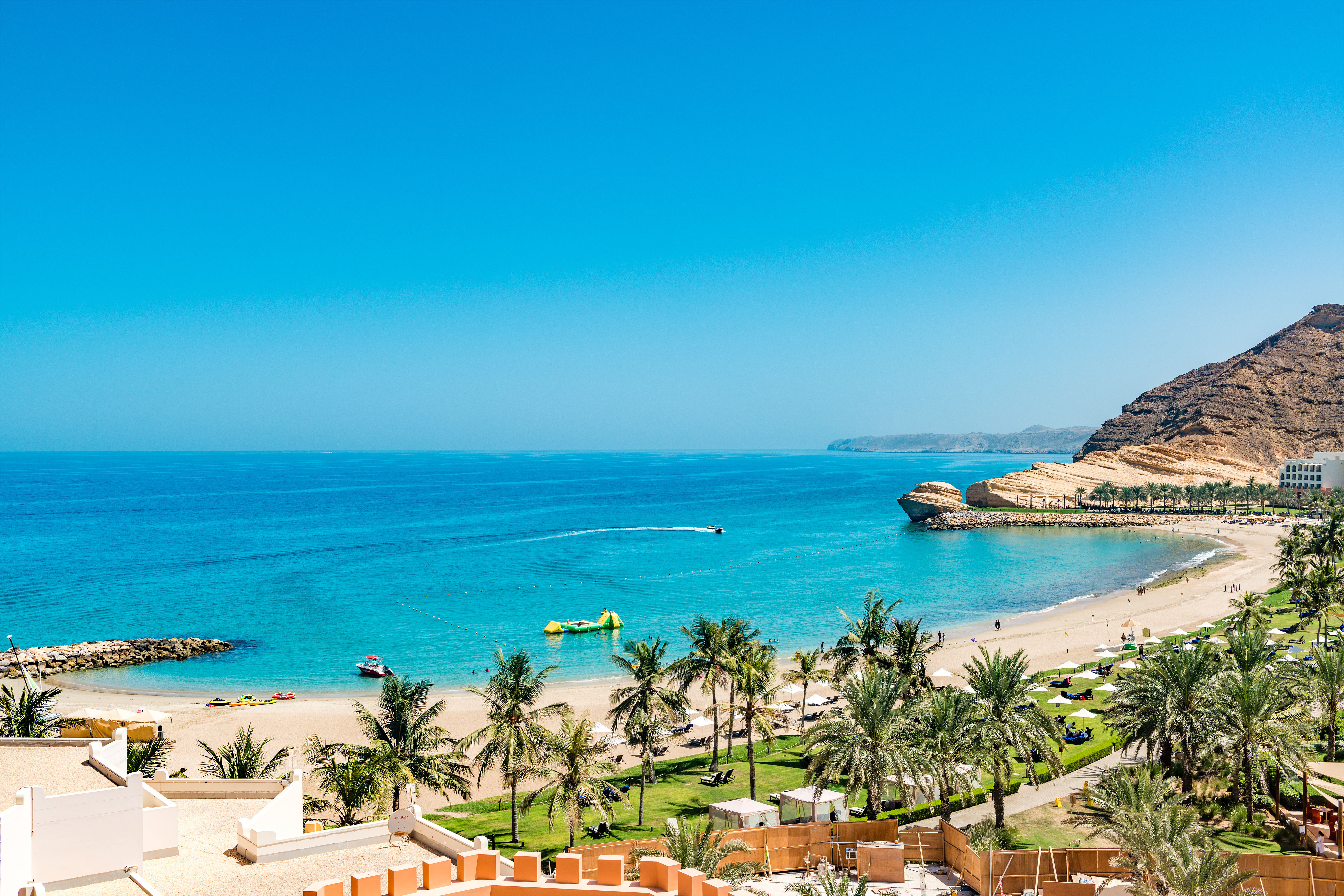 Beautiful golden sand beach with green trees, mountains and blue sea and sky in Oman.