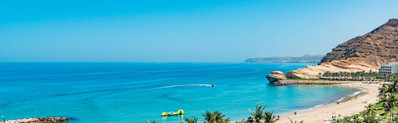 Beautiful golden sand beach with green trees, mountains and blue sea and sky in Oman.