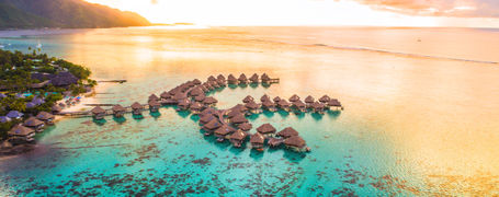 Colourful sunset over shallow reef lagoon with water bungalow resort in French Polynesia.