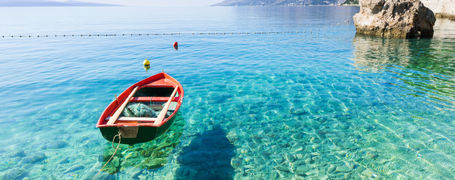 Small red boat on crystal clear waters in beautiful bay in Croatia.