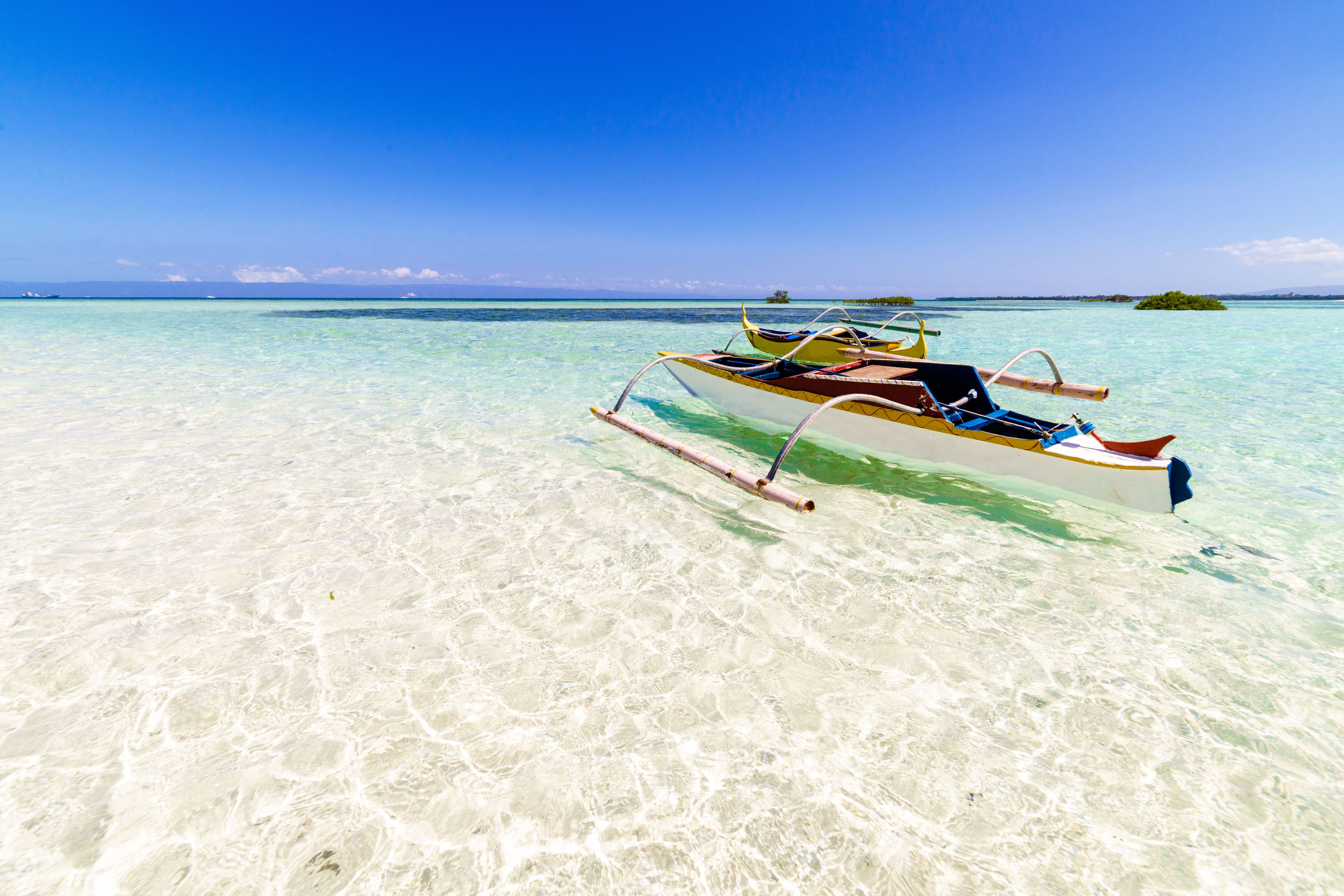 Traditional white fishing boat on crystal clear water over white sand and blue sky in Panglao, Philippines. 