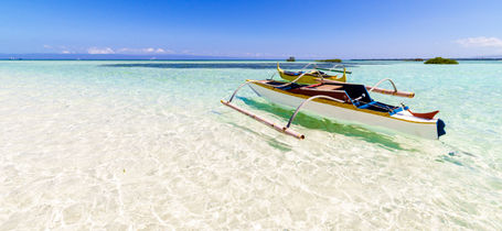 Traditional white fishing boat on crystal clear water over white sand and blue sky in Panglao, Philippines. 