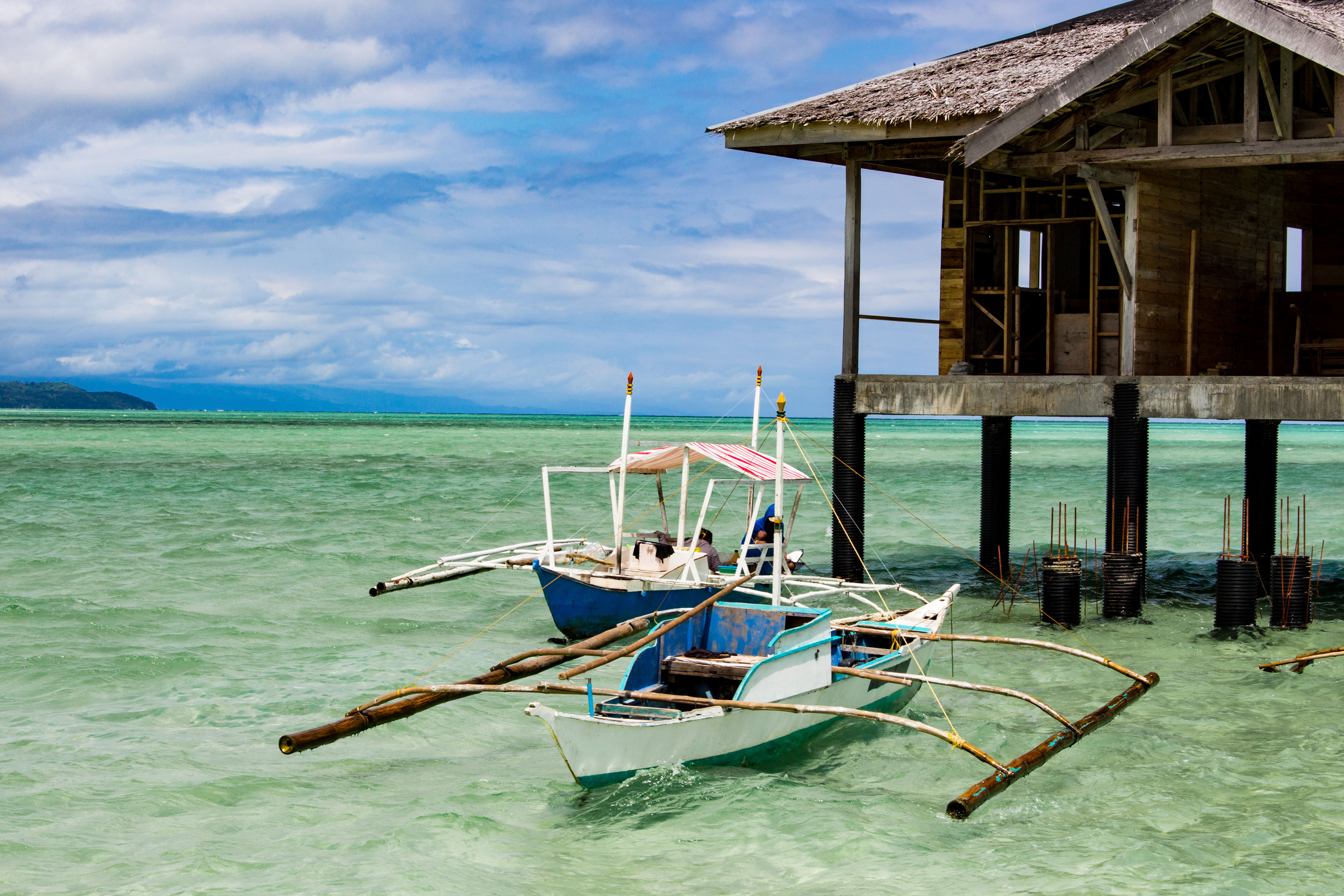 Traditional wooden boat next to hut on stilts over crystal clear water in Negros, Philippines. 