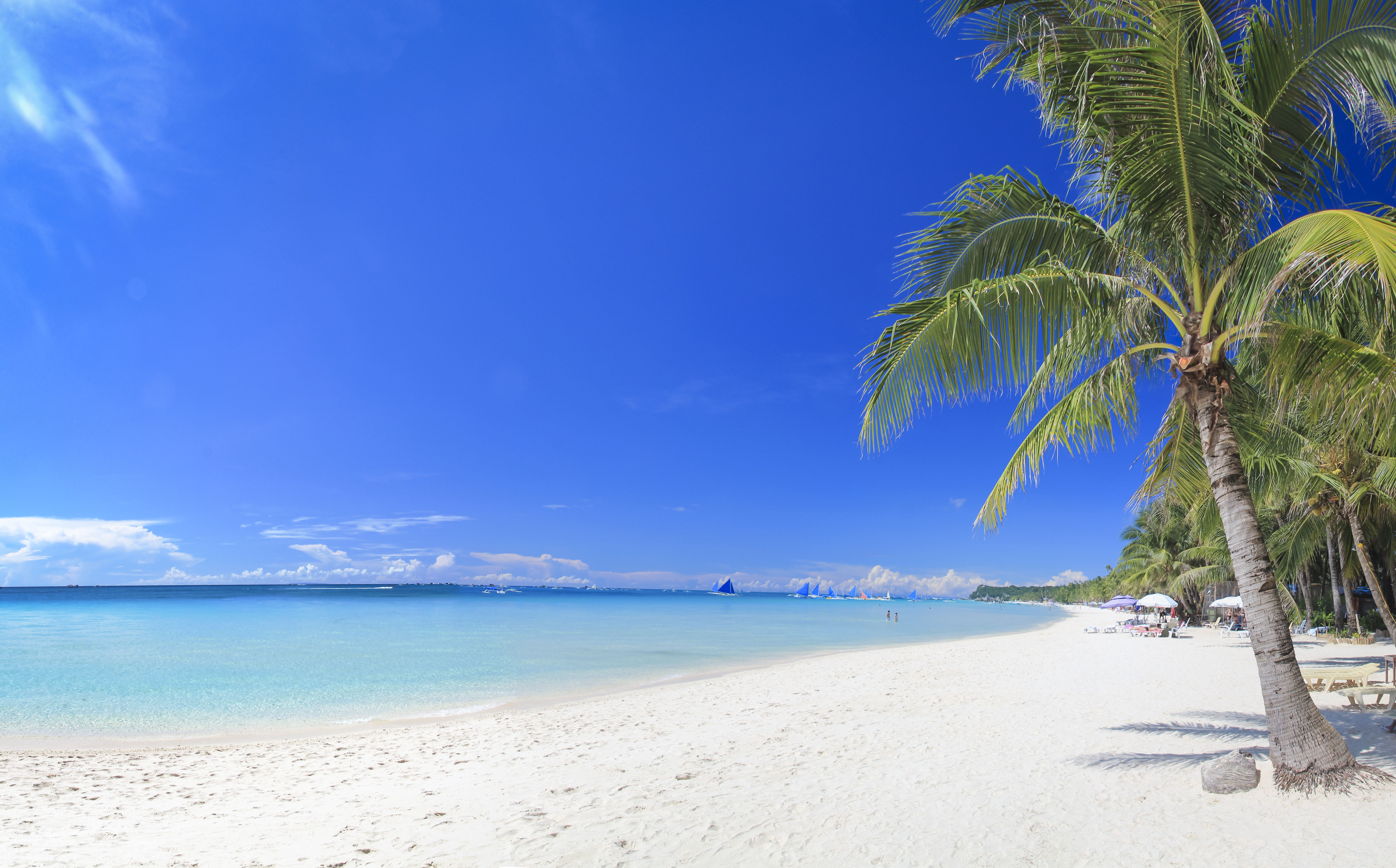 Stunning white sand beach with palm trees and crystal clear blue waters in Boracay, Philippines. 