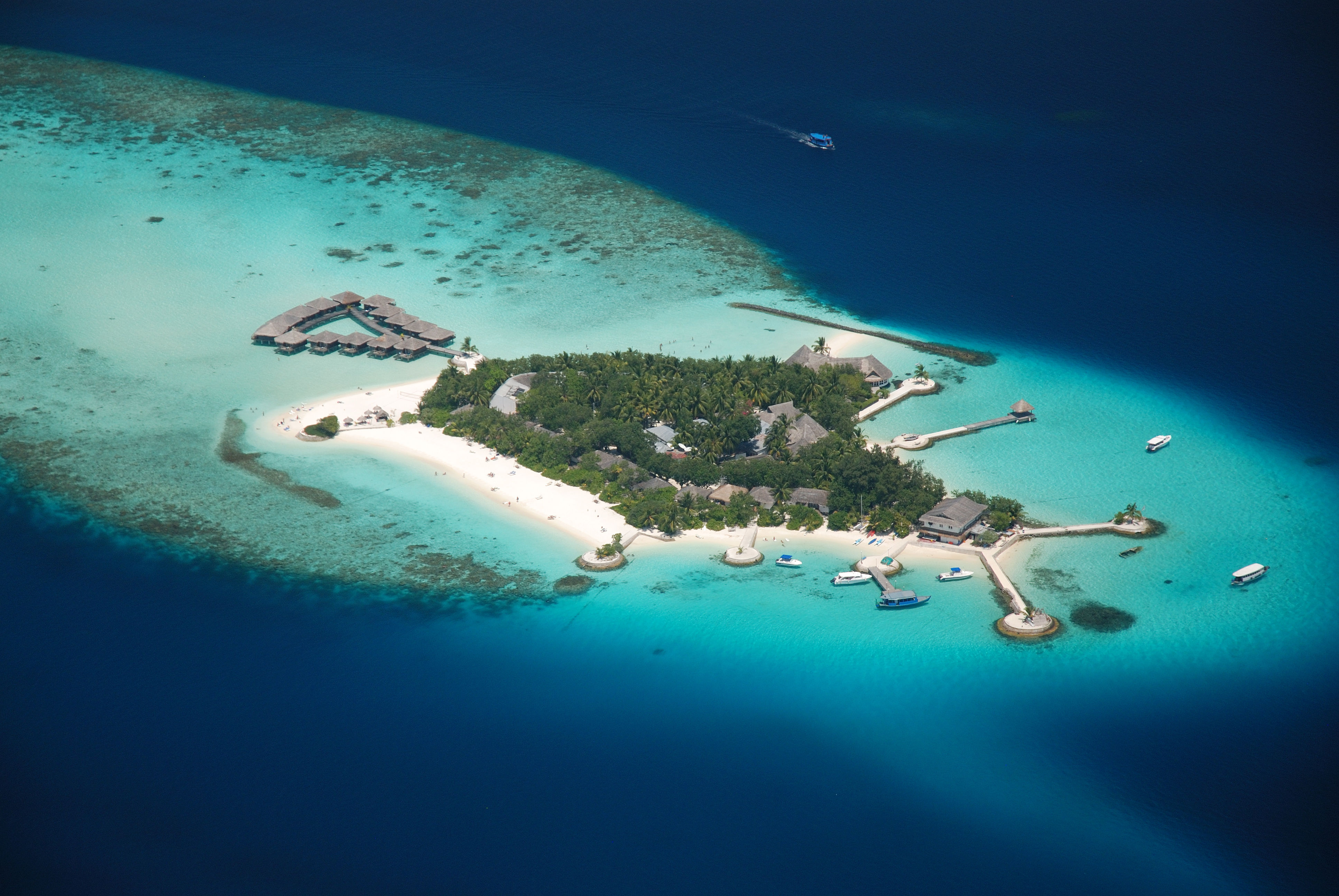 Aerial view of remote island in Maldives, with resort bungalows, turquoise waters and white sand beaches. 