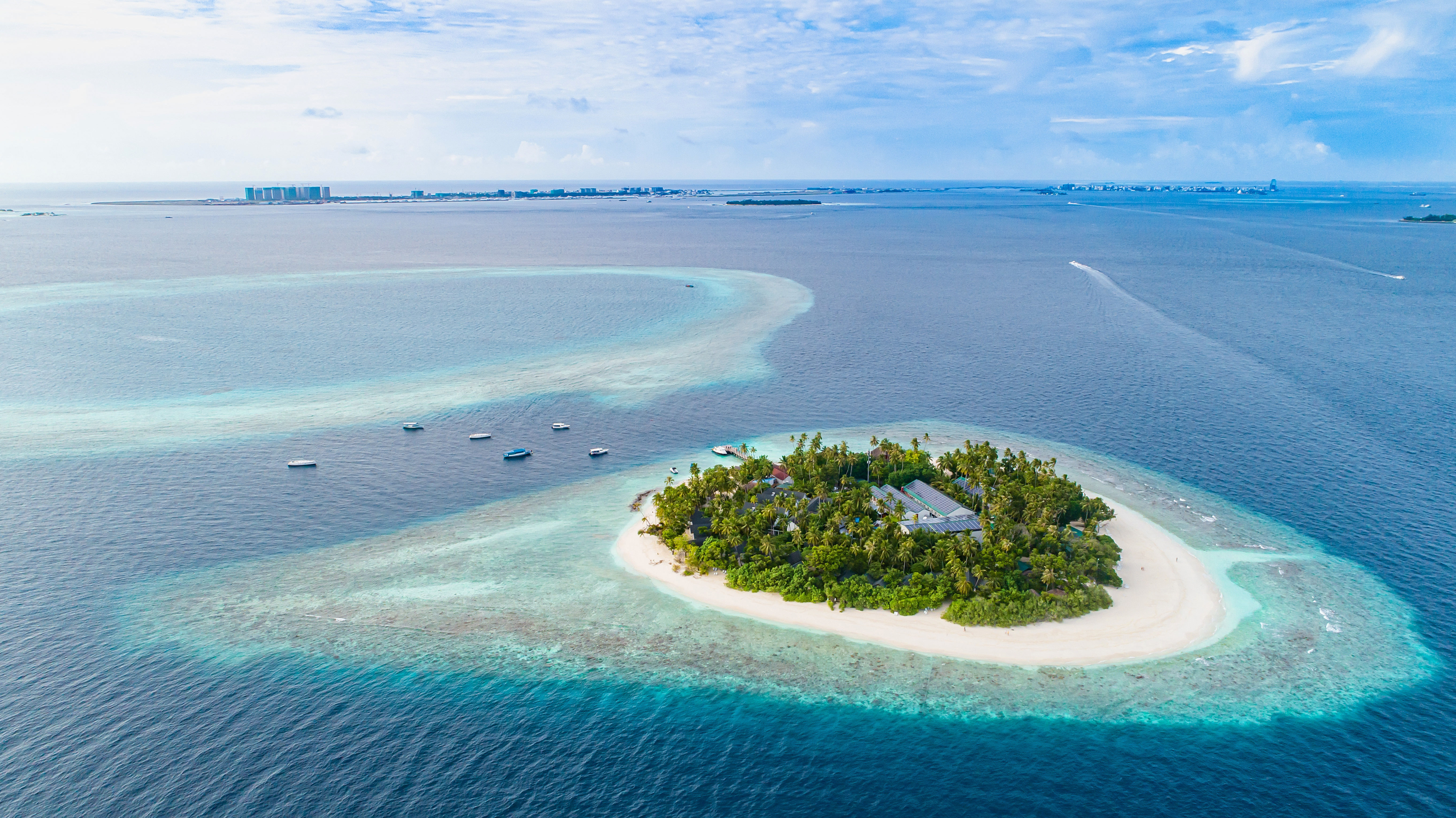 Aerial drone view of Maldives atoll island with resort, tropical green trees, shallow reefs and aqua blue waters. 