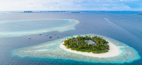 Aerial drone view of Maldives atoll island with resort, tropical green trees, shallow reefs and aqua blue waters. 
