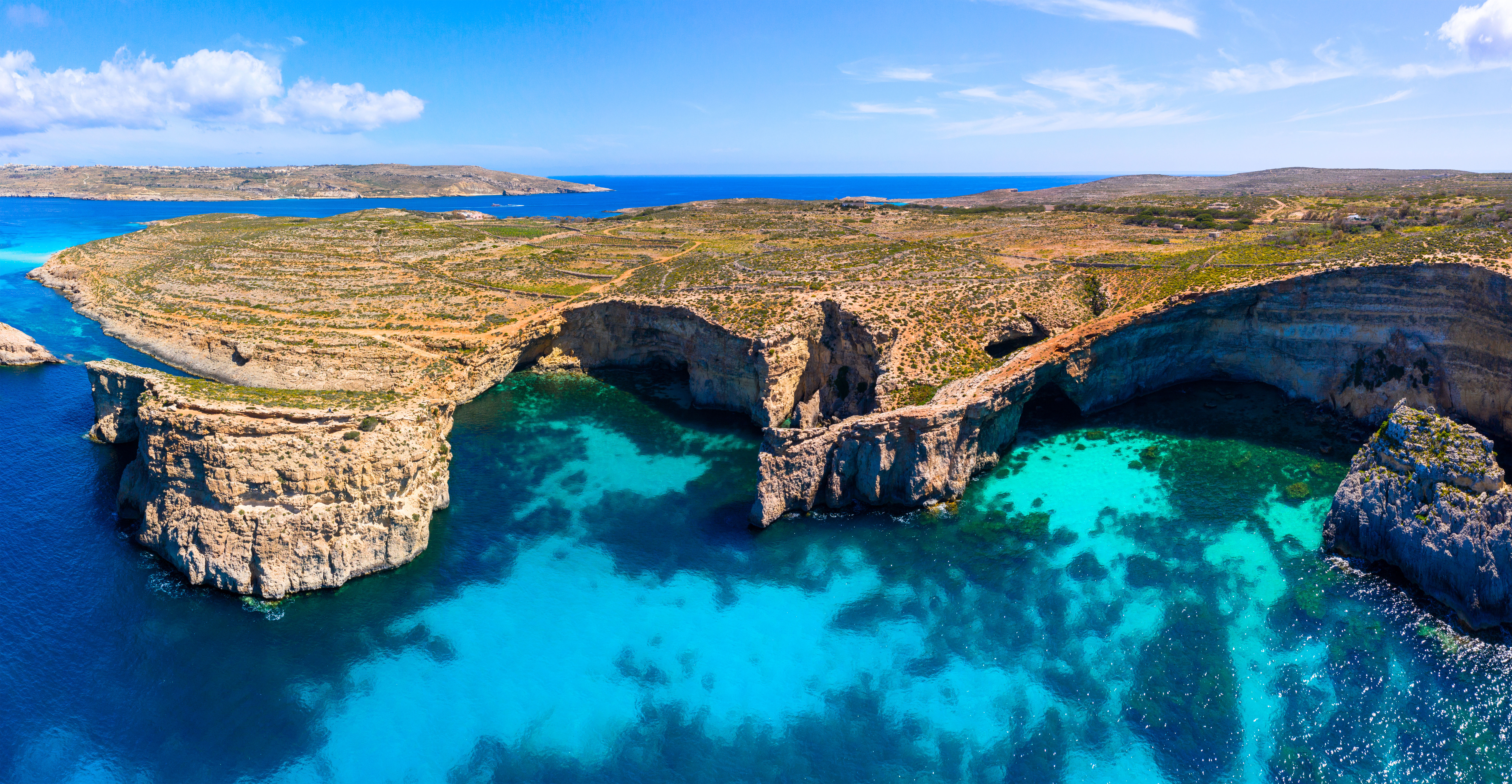 Aerial drone view of Comino Island caves next to crystal clear turquoise waters in Malta