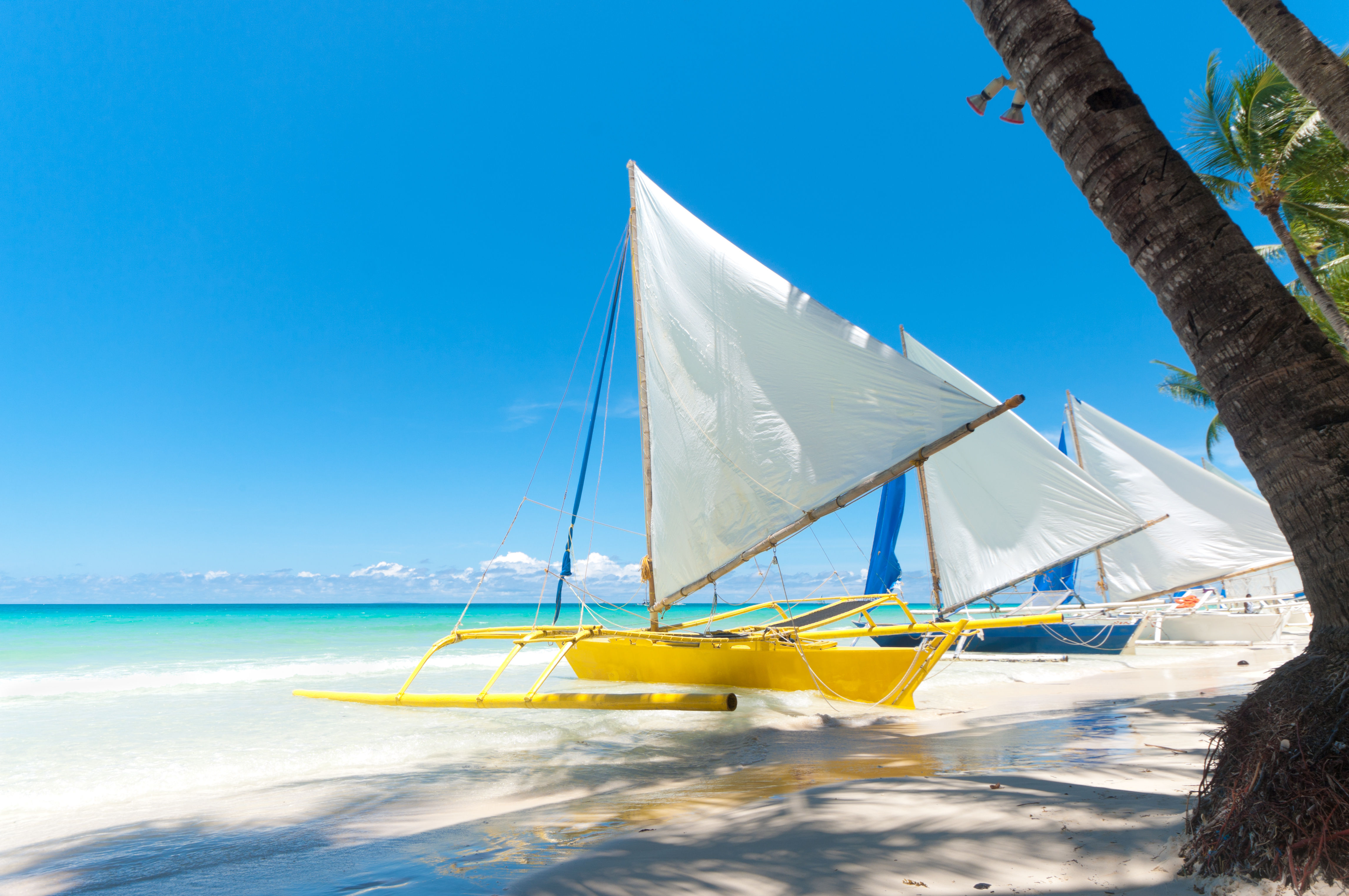 Colorful traditional Filipino boats on white sand shore, near crystal clear turquoise water in Visayas. 