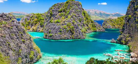 Limestone Islands surrounded by clear blue and turquoise waters and moored Filipino boats in Palawan. 