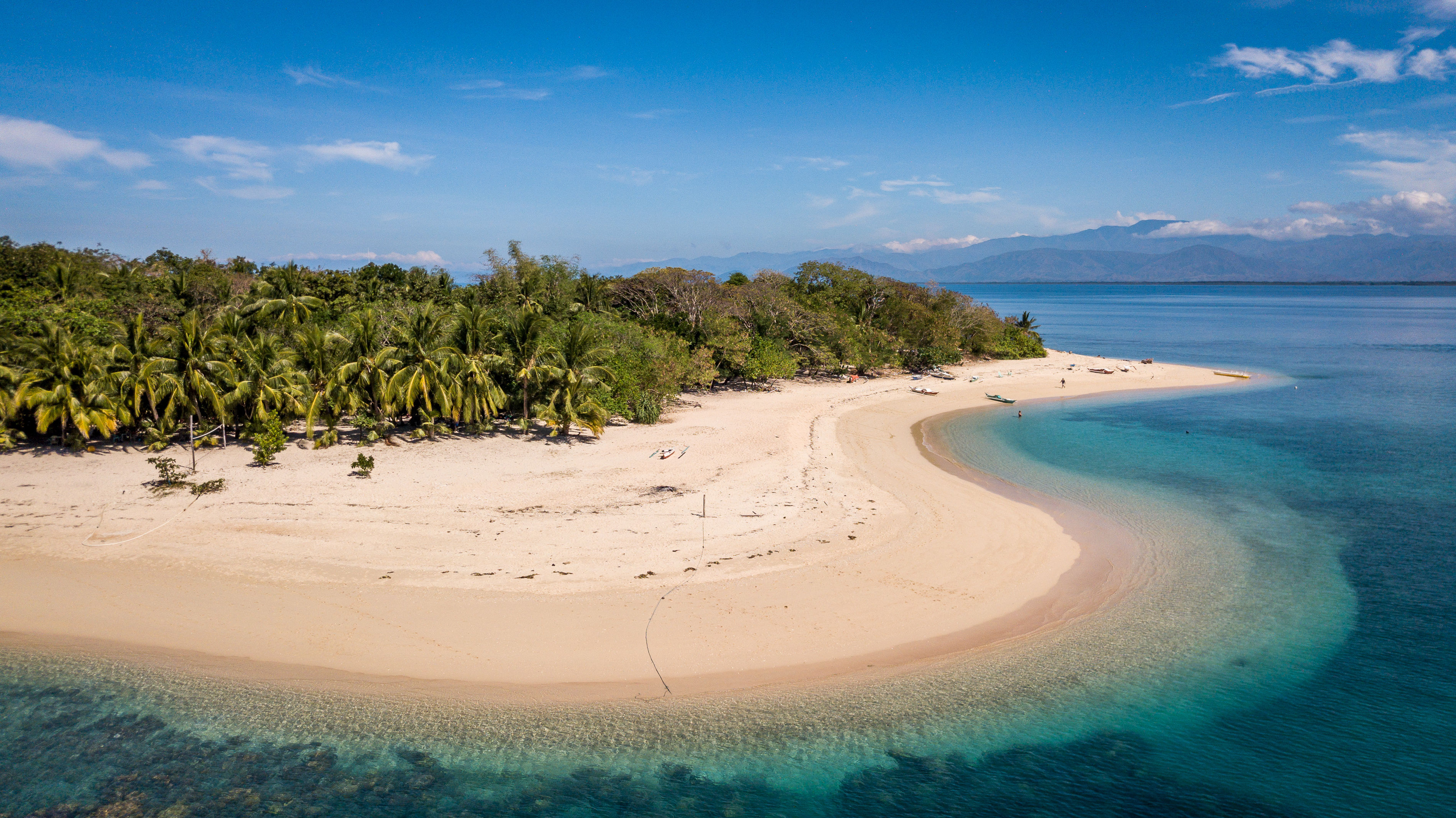 Aerial view of white sand tropical island of Mindoro with green palm trees and surrounded by clear turquoise waters, Philippines. 