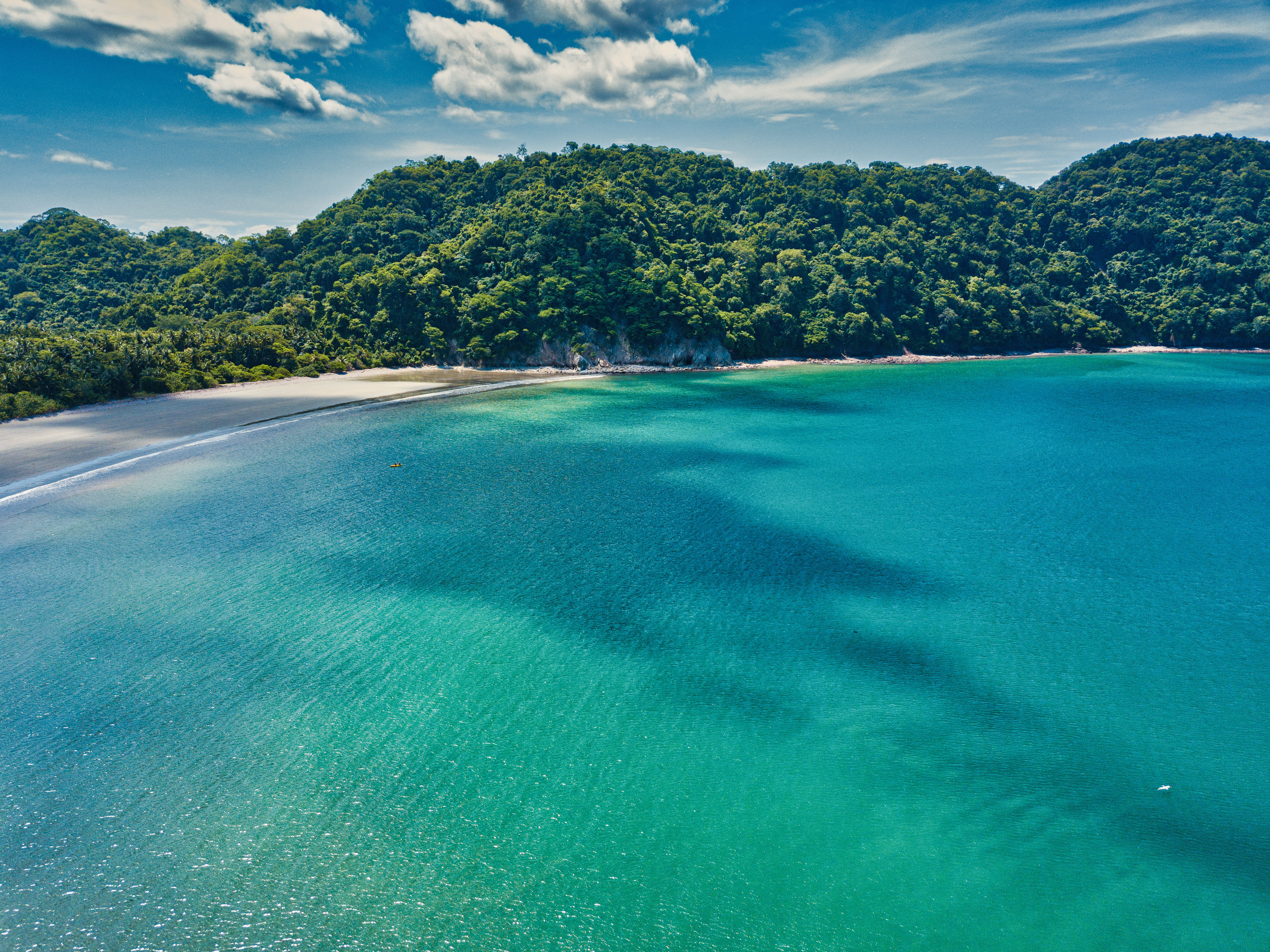 An empty, beautiful white sand beach around the Gulf of Nicoya in Costa Rica with lush green hills and turquoise waters.